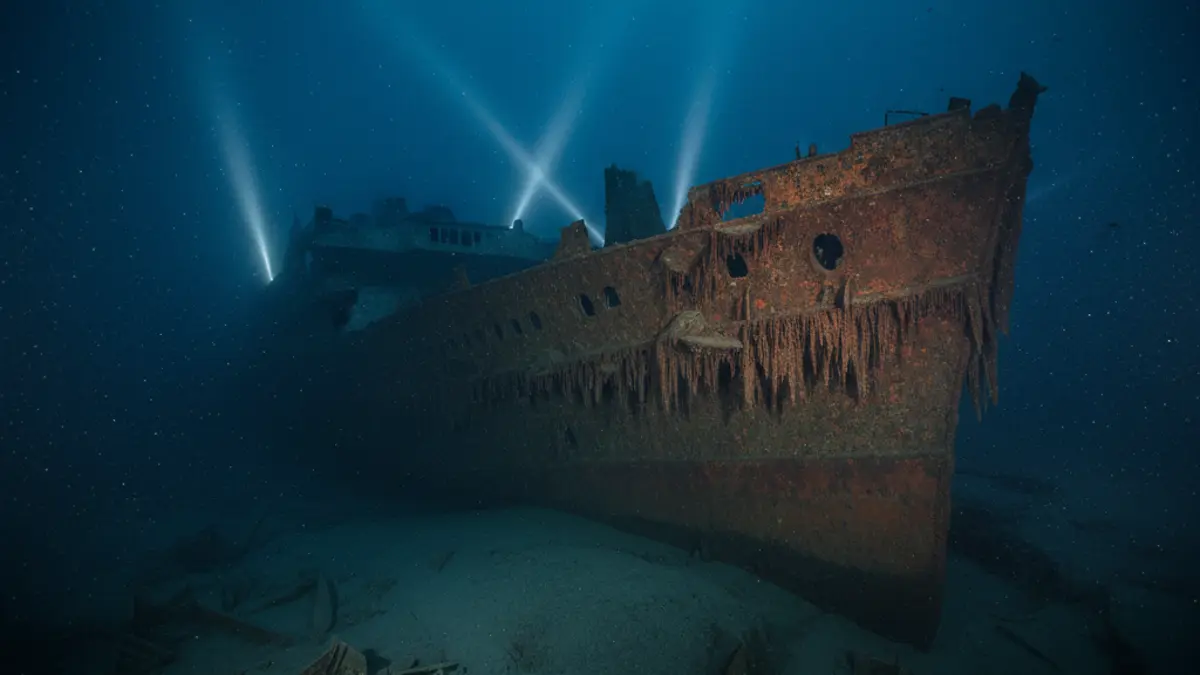 Das Wrack der Titanic am Meeresgrund, der rostige Bug wird von den Scheinwerfern eines U-Boots aus der Dunkelheit beleuchtet.